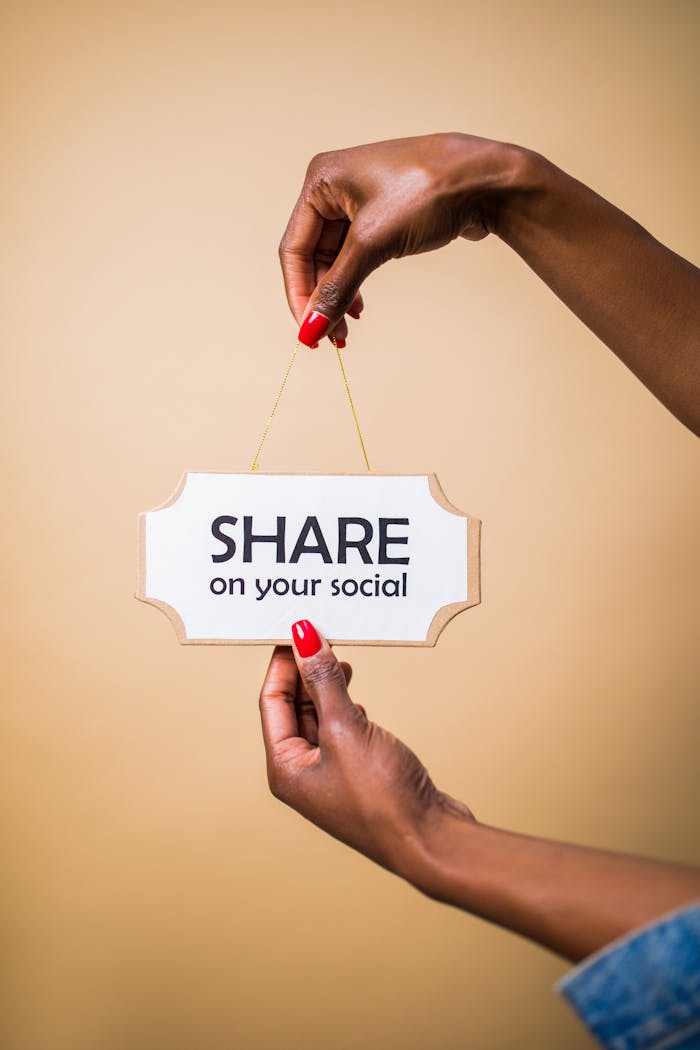 Close-up of a persons hand holding a Share on your social sign against a beige background.